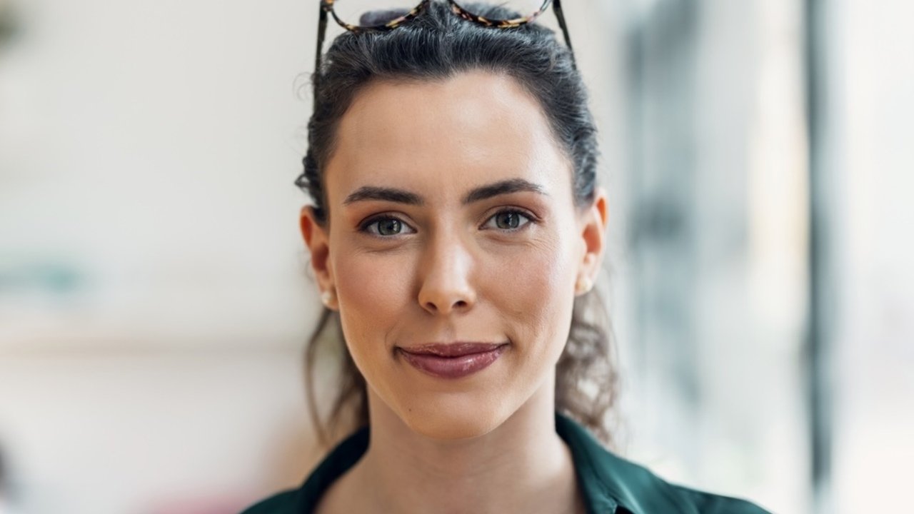 Sebavedomá mladá žena s okuliarmi na hlave, ktorá pôsobí premýšľavo a inteligentne.