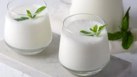 Poháre čerstvého kefiru ozdobené lístkami mäty na svetlom stole.