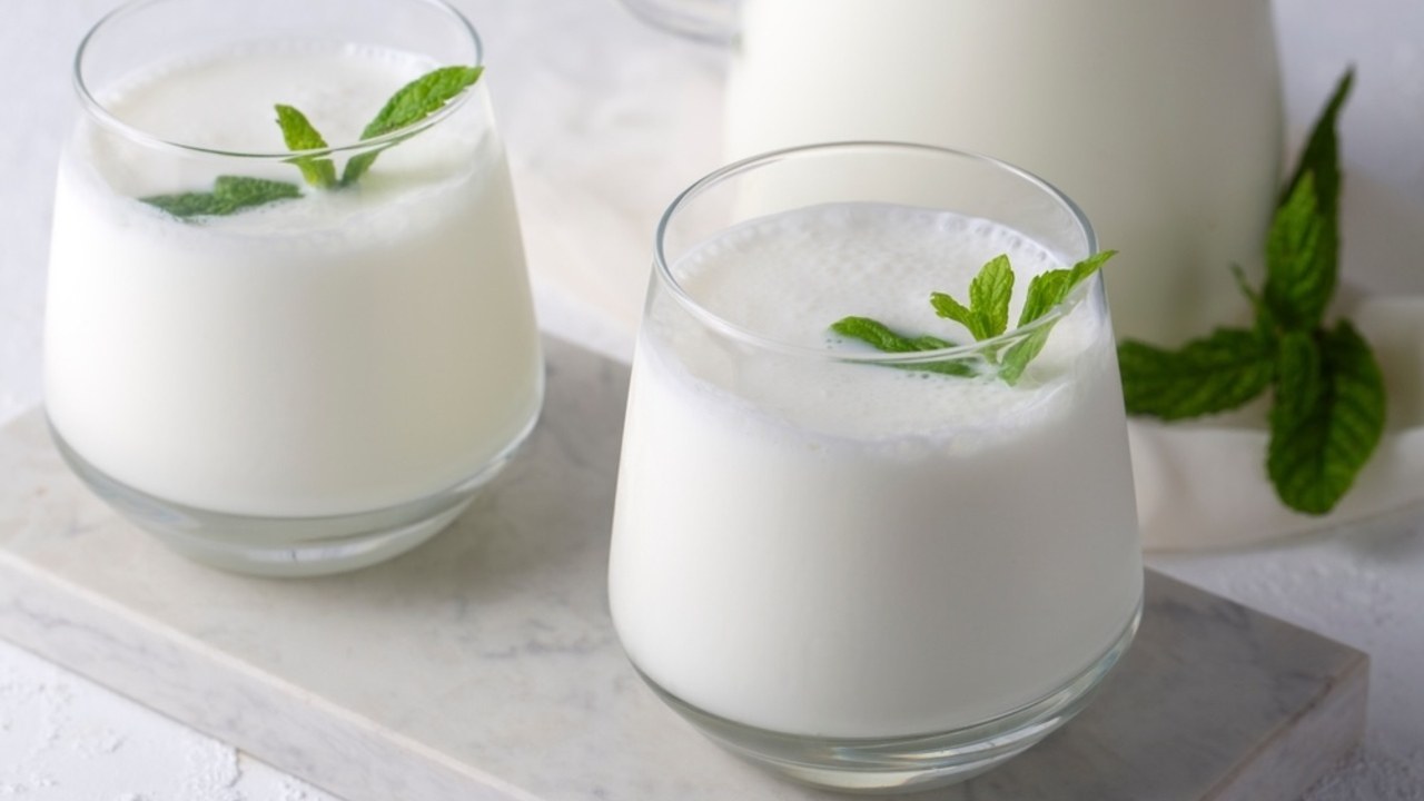 Poháre čerstvého kefiru ozdobené lístkami mäty na svetlom stole.