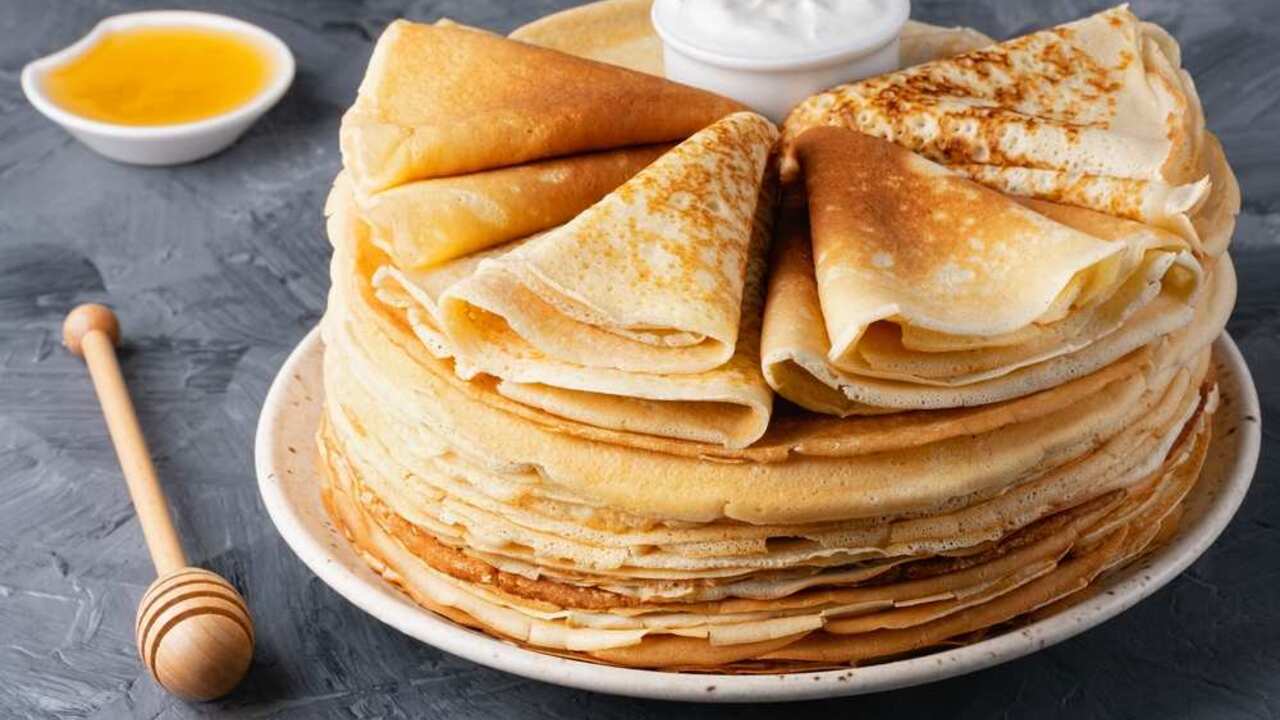 Veľká kôpka tenkých palaciniek poskladaných do trojuholníkov, podávaná s medom a smotanou.