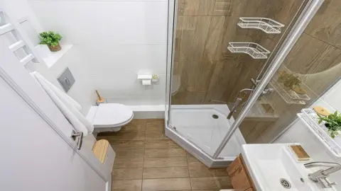Svetlá malá kúpeľňa s preskleným sprchovým kútom, drevenou podlahou a minimalistickým zariadením, ktoré opticky zväčšujú priestor.