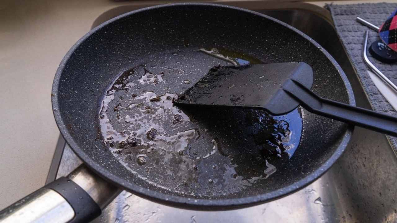 Panvica s olejom umývaná pod tečúcou vodou v kuchynskom dreze.