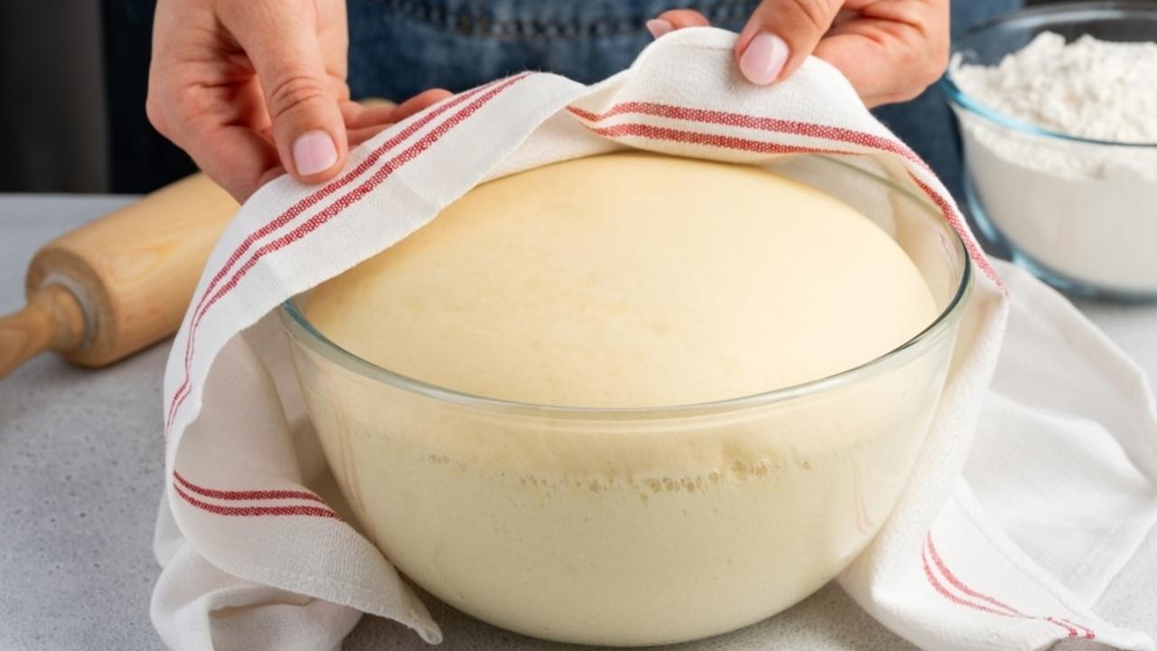 Nadýchané kvasnicové cesto kysnúce v miske zakryté utierkou