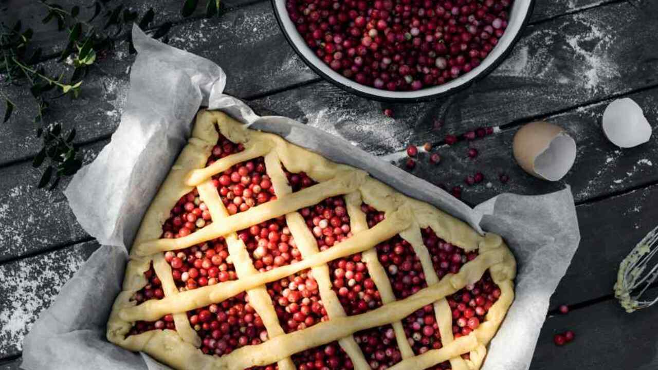 Domáci krehký koláč s brusnicami v plechu pred pečením, pripravený na rustikálnom stole