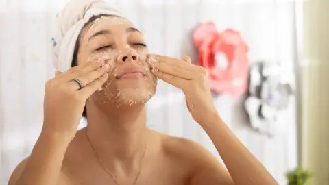Žena nanáša domácu pleťovú masku z ovsených vločiek a medu na tvár v kúpeľni