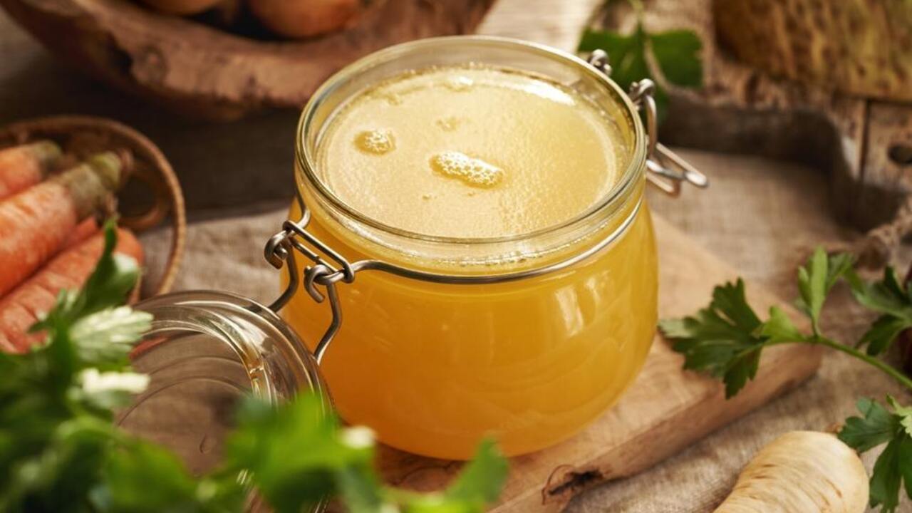 Domáci zlatistý vývar v sklenenom pohári s mastnými očkami na povrchu