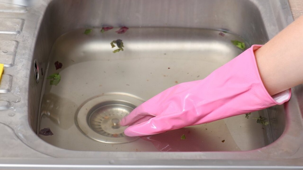 Upchatý kuchynský drez so stojacou vodou a rukou v ružovej rukavici pri odtoku