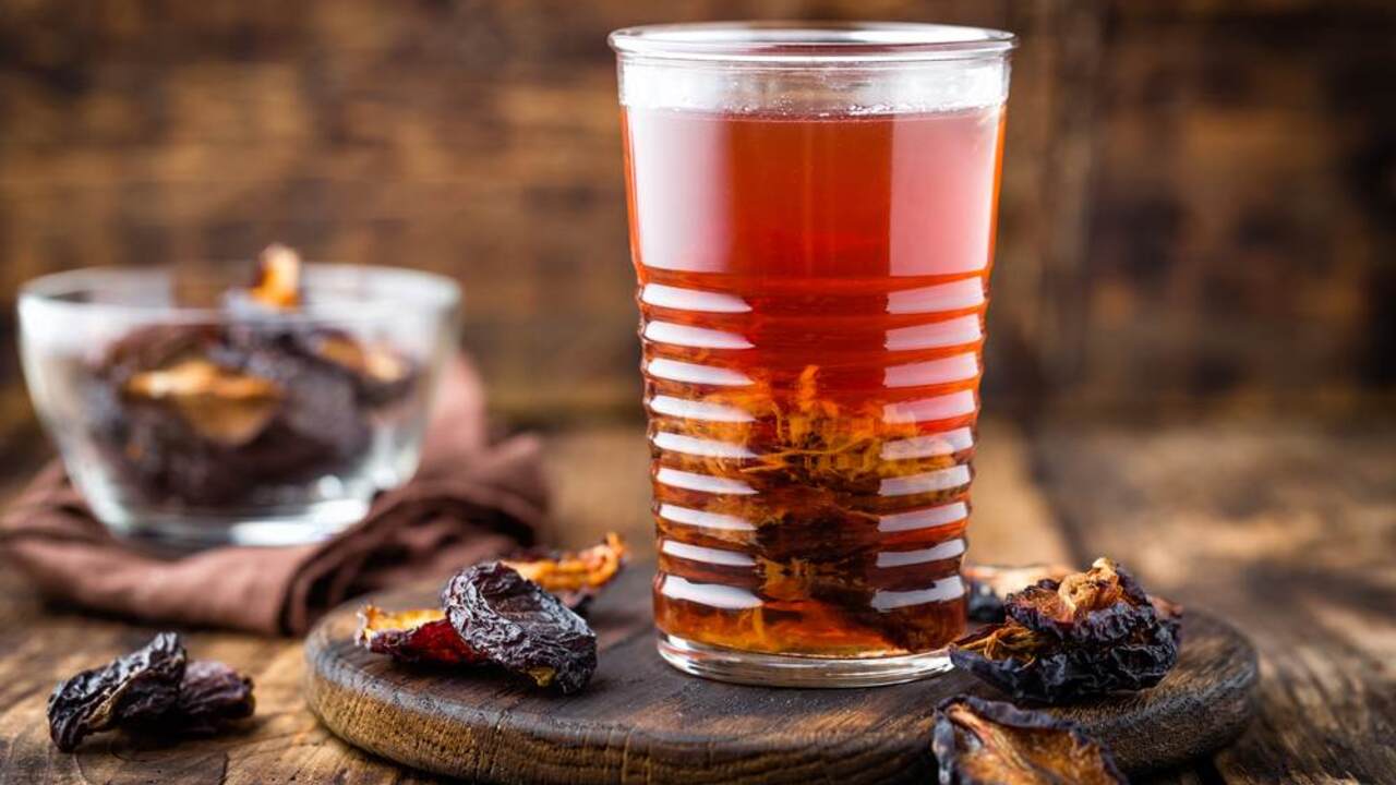 Pohár vody zo sušených sliviek s namočenými kúskami ovocia na drevenom stole