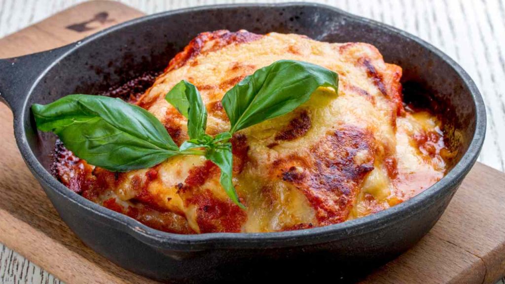 Lasagne v liatinovej panvici na drevenej doske. Tradičné talianske jedlo