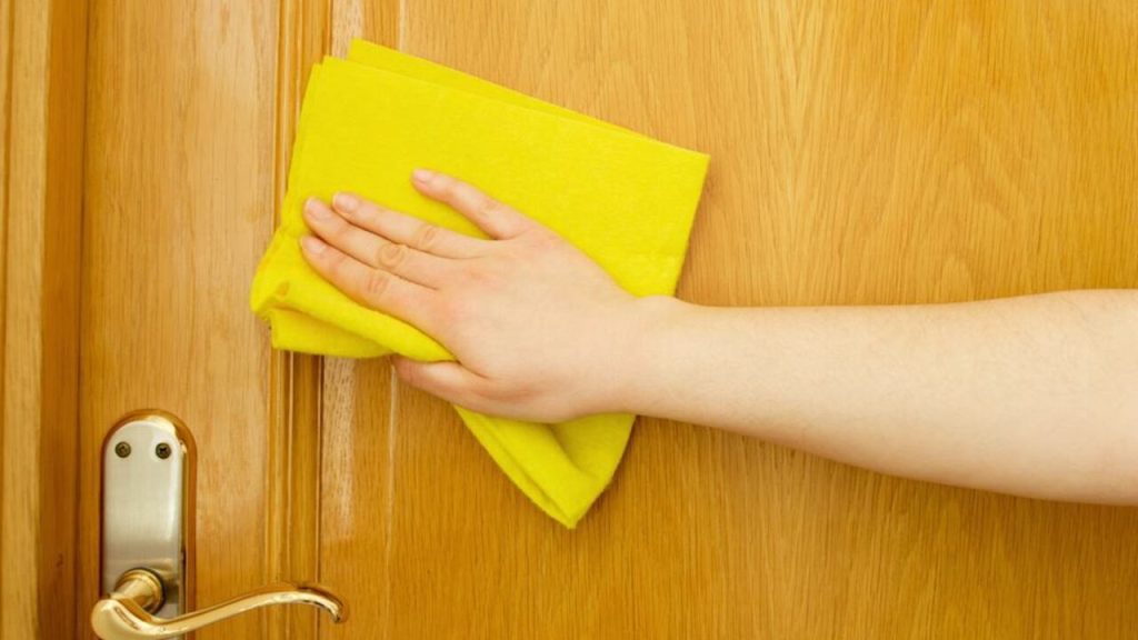 Ruka utiera lakované drevené dvere žltou handričkou z mikrovlákna