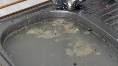 Upchatý kuchynský drez s pomaly odtekajúcou vodou a zvyškami jedla