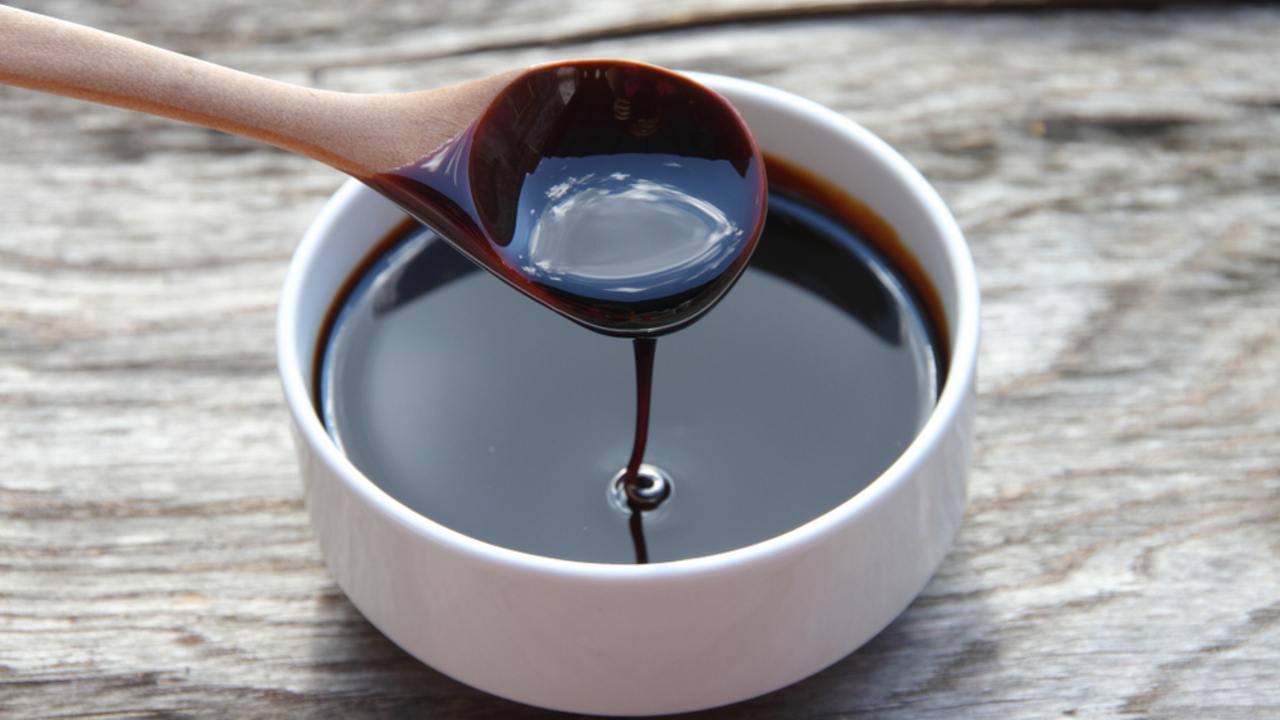 Tmavá melasa v lyžičke nad pohárom ako prírodné sladidlo