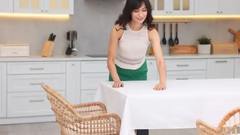 Žena upravuje biely obrus na stole v modernej kuchyni