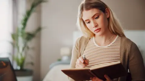 Mladá žena si zapisuje poznámky do zápisníka v tichom domácom prostredí