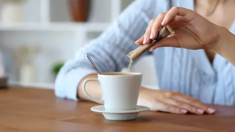 Žena si doma sype cukor do kávy