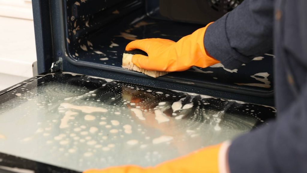 Žena v kuchyni čistí rúru špongiou, detailný záber