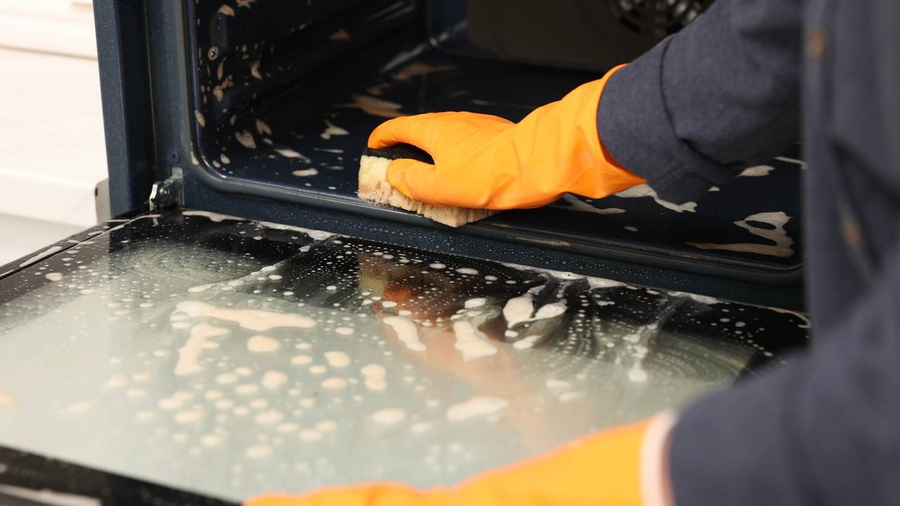 Žena v kuchyni čistí rúru špongiou, detailný záber
