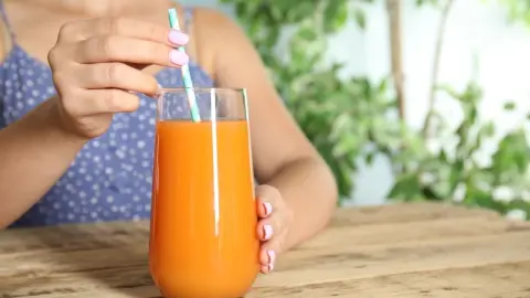 Žena s pohárom čerstvo vylisovanej mrkvovej šťavy pri drevenom stole, detailný záber