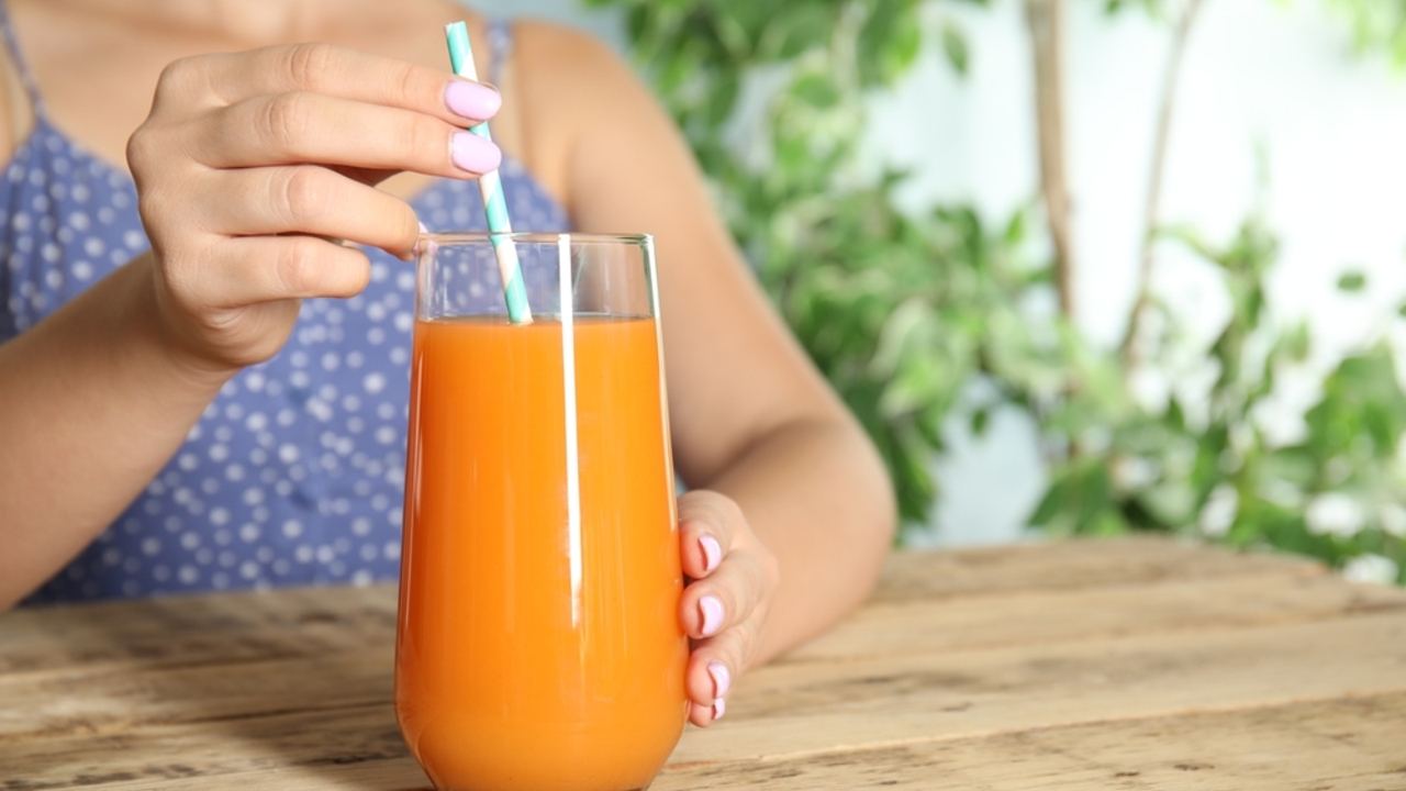 Žena s pohárom čerstvo vylisovanej mrkvovej šťavy pri drevenom stole, detailný záber