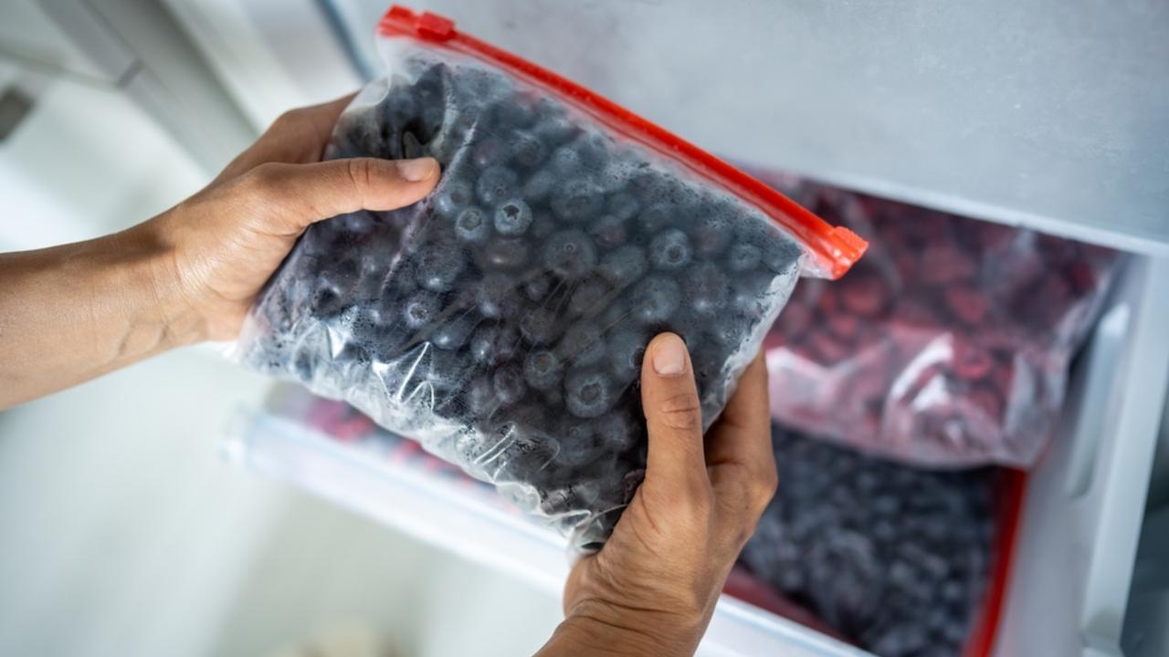 Žena drží v rukách vrecúško na zips s čučoriedkami a vkladá ho do mrazničky. Cenovo výhodné skladovanie potravín, konzervovanie letného ovocia na zimu, vitamíny na chladné obdobie, rýchle zmrazenie, výživové výhody