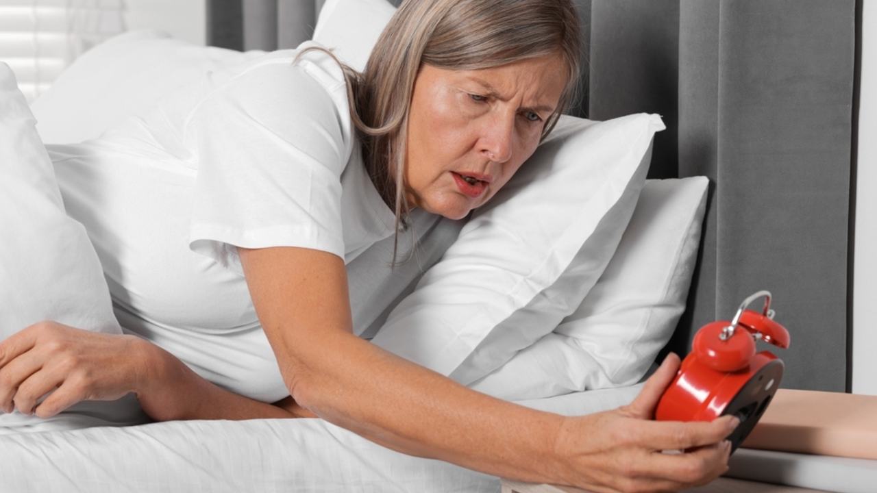 Žena, ktorá nevie zaspať, s budíkom v posteli doma