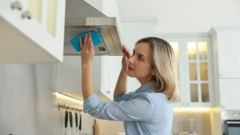 Žena, ktorá v interiéri čistí kuchynský odsávač pary digestor handričkou
