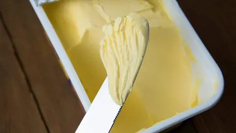 Rastlinné maslo v plastovej nádobe s nožom, maslo na varenie a na sendviče.