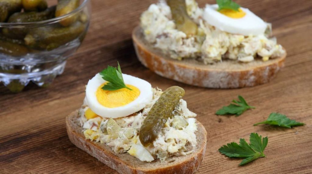 Rybia paštéta na tmavom chlebe s vajcom a nakladanými uhorkami. Domáca nátierka zo sardiniek, vajec, tvarohu a nakrájaných nakladaných uhoriek.