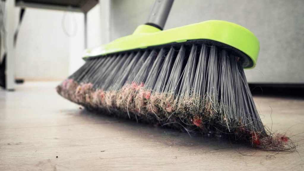 Plastová metla s prachom a nečistotami, stojaca na drevenej podlahe v domácnosti alebo v kancelárii. Koncepcia upratovacích služieb a domácich prác.