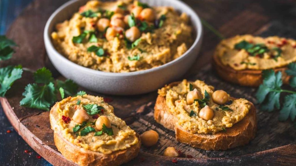 Hummus, cícerová kaša v miske a na opečených krajcoch chleba na modrom drevenom pozadí
