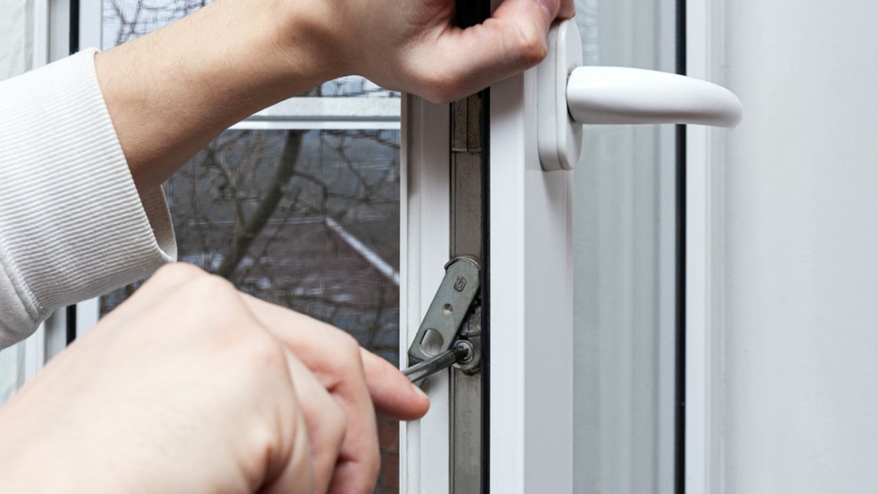 Montáž, nastavenie a údržba plastových okien z PVC. Údržbár otvoril a nastavil plastové okno v dome. Nastavenie uzamykacieho mechanizmu pomocou skrutkovača.