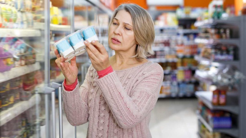 Prekvapená žena číta etiketu na výrobku pri výbere potravín v supermarkete
