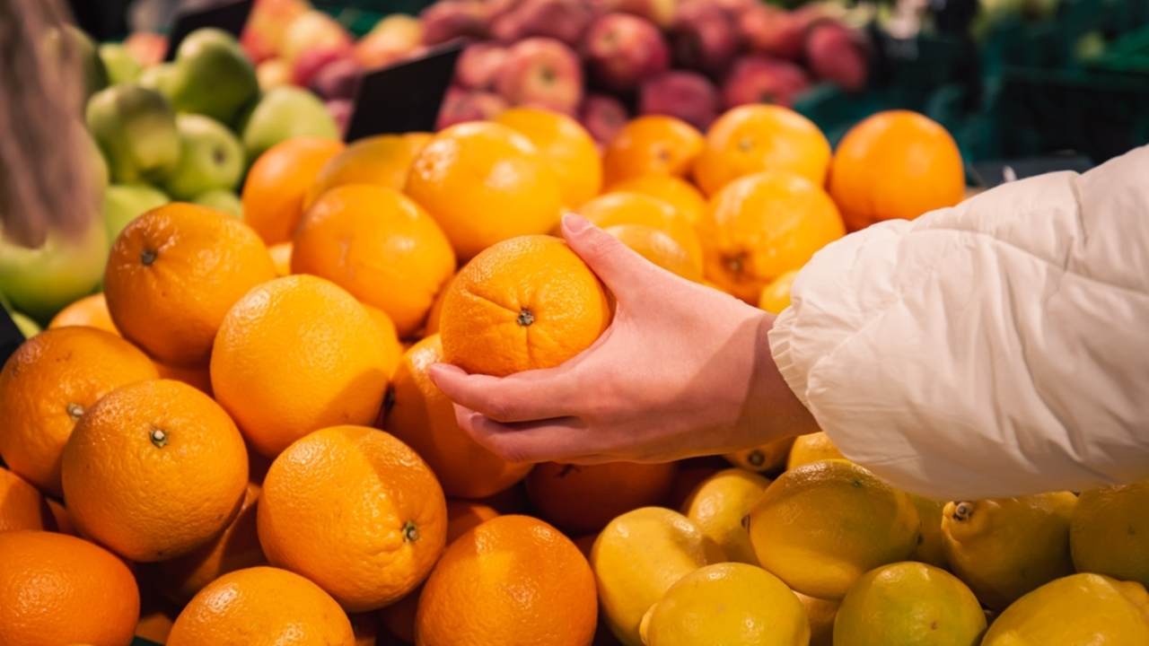 Záber zblízka na ženu, ktorá si v obchode s potravinami vyberá pomaranče.