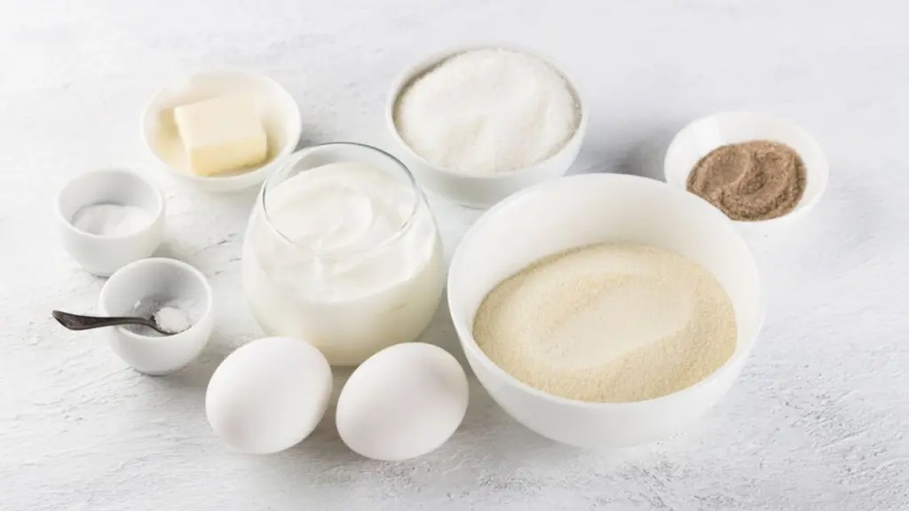Ingrediencie na prípravu lahodného koláča z krupice: krupica, vajcia, kyslá smotana alebo jogurt, cukor, vanilkový cukor, maslo, soľ, sóda na svetlosivom pozadí