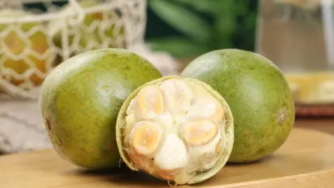 Čerstvé ovocie monk fruit z Guilinu vystavené na drevenej doske spolu s tradičným tkaným košíkom, čím sa zdôrazňuje toto sladké prírodné ovocie, obľúbené v ázijskej kuchyni a v bylinných čajoch