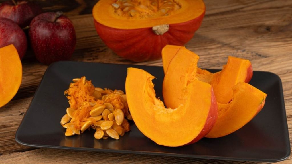 Plátky tekvice Red Kuri alebo tekvice Hokkaido na drevenom stole. Zimná tekvica s tenkou šupkou a oranžovou farbou, kúsky sladkej zimnej tekvice Hokkaido na rustikálnom pozadí